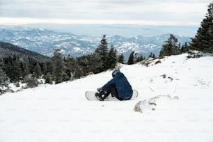 a snowboarder is sitting on a snowy mountain