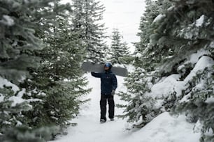 a man holding a snowboard in the middle of a forest