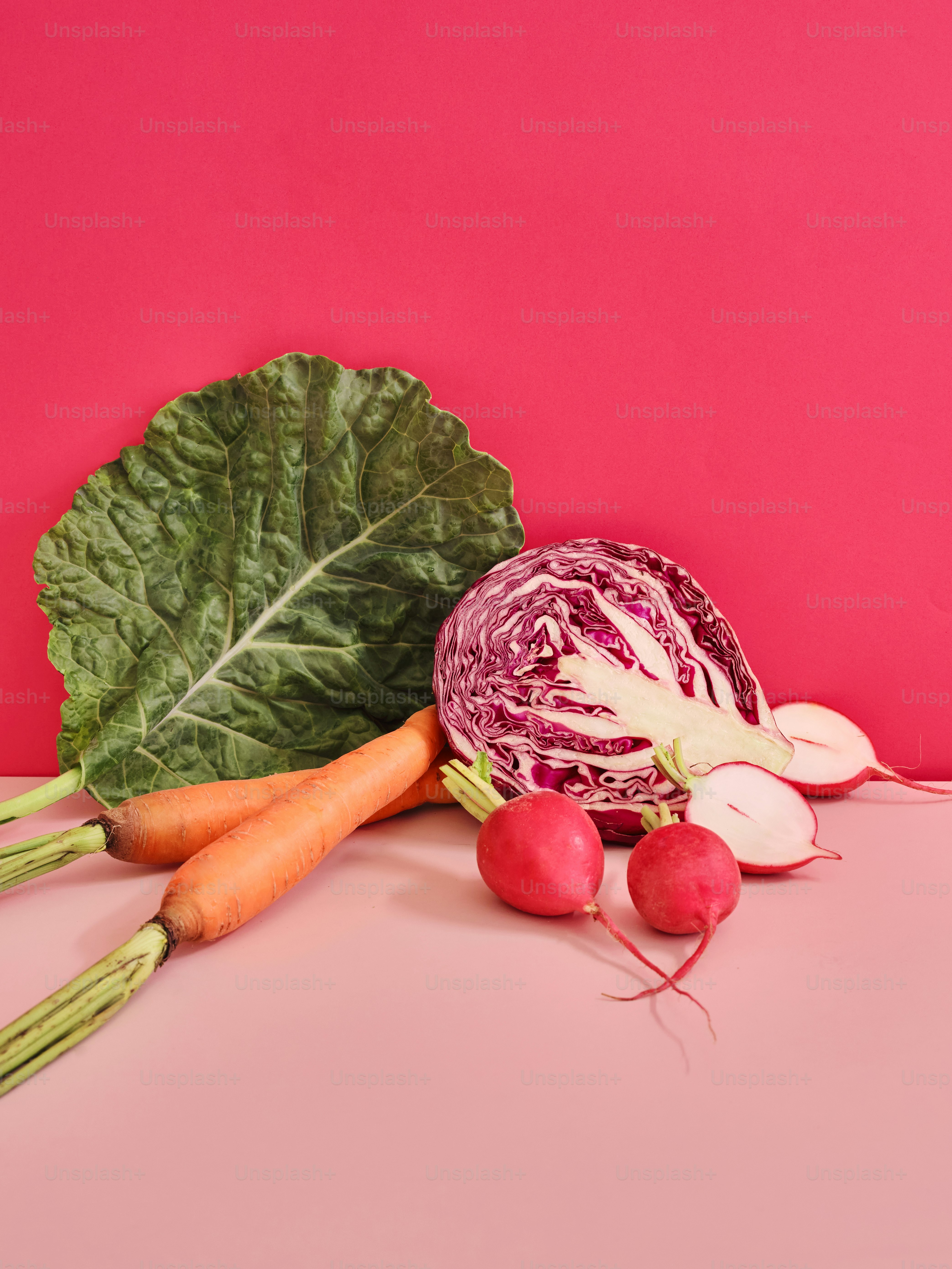 a cabbage, radishes, and carrots on a pink surface