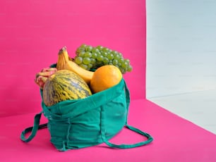 un sac vert rempli de fruits sur fond rose