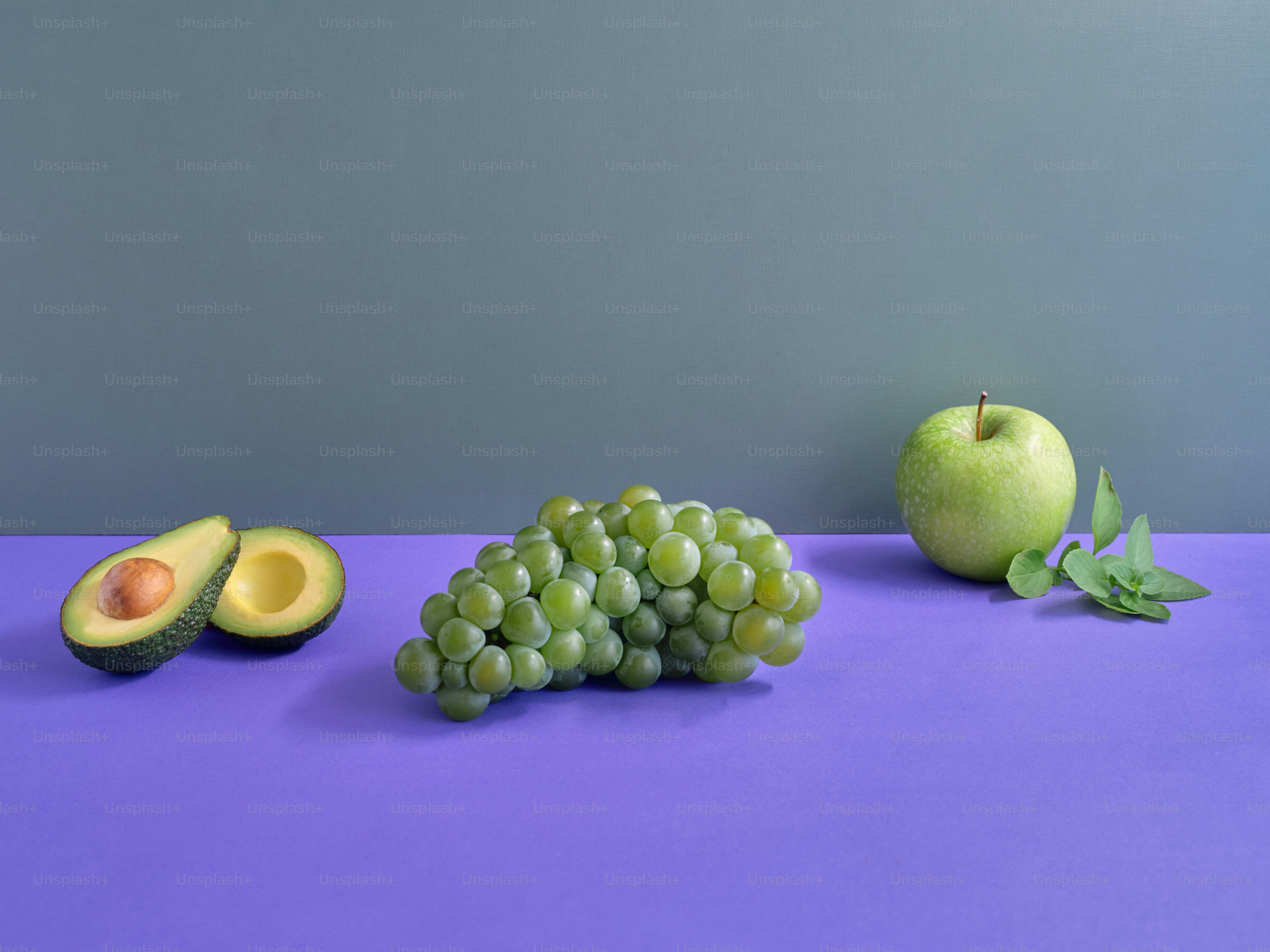 a purple table topped with green fruit and an avocado