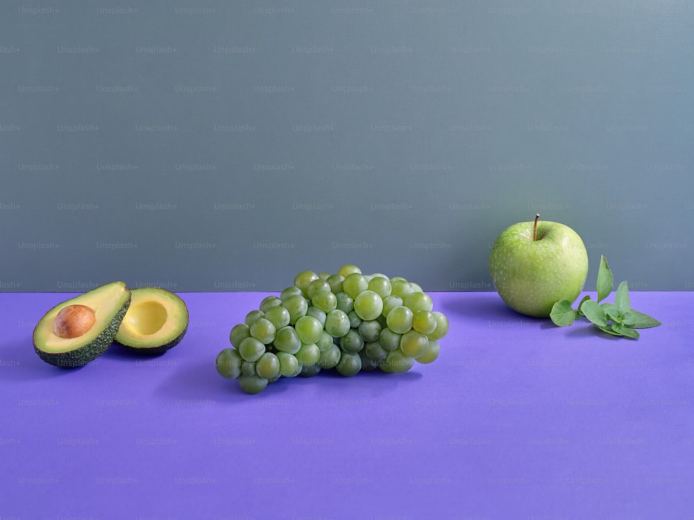 ein lilafarbener Tisch mit grünen Früchten und einer Avocado