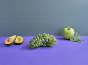 a purple table topped with green fruit and an avocado