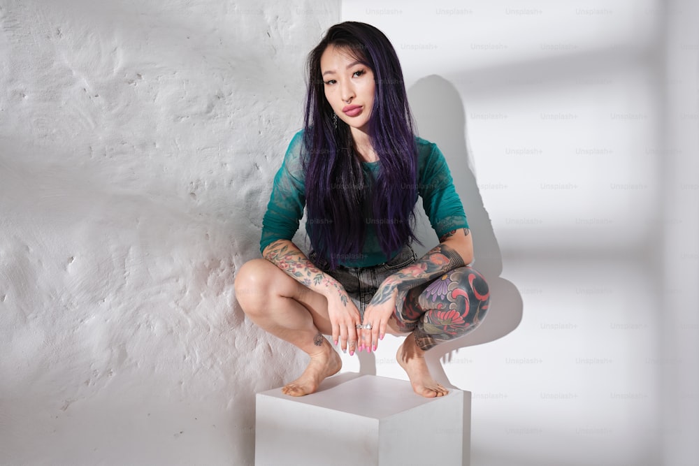a woman with tattoos sitting on top of a white cube