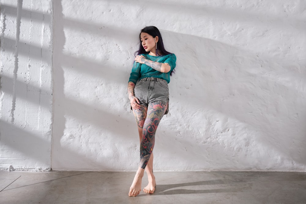 a woman with tattoos standing in front of a white wall