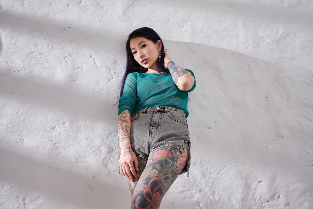 a woman with tattoos is leaning against a wall