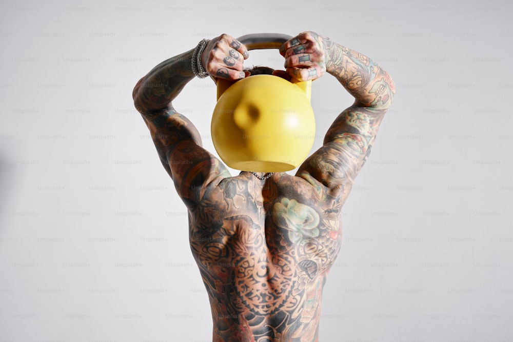 un homme tatoué tenant une cruche jaune au-dessus de sa tête