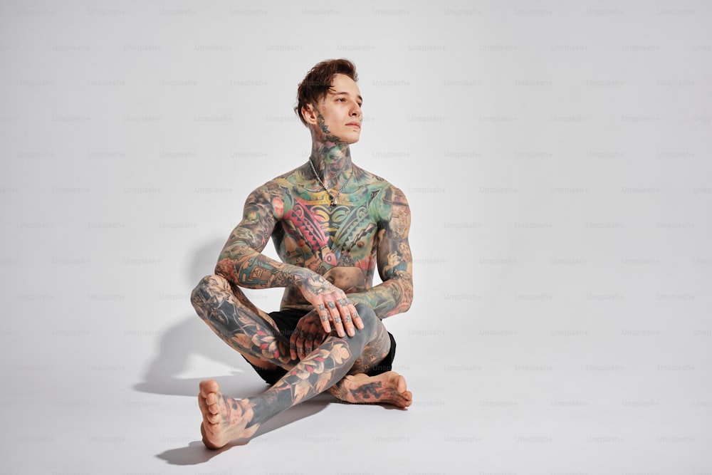 a tattooed man sitting on the ground with his legs crossed