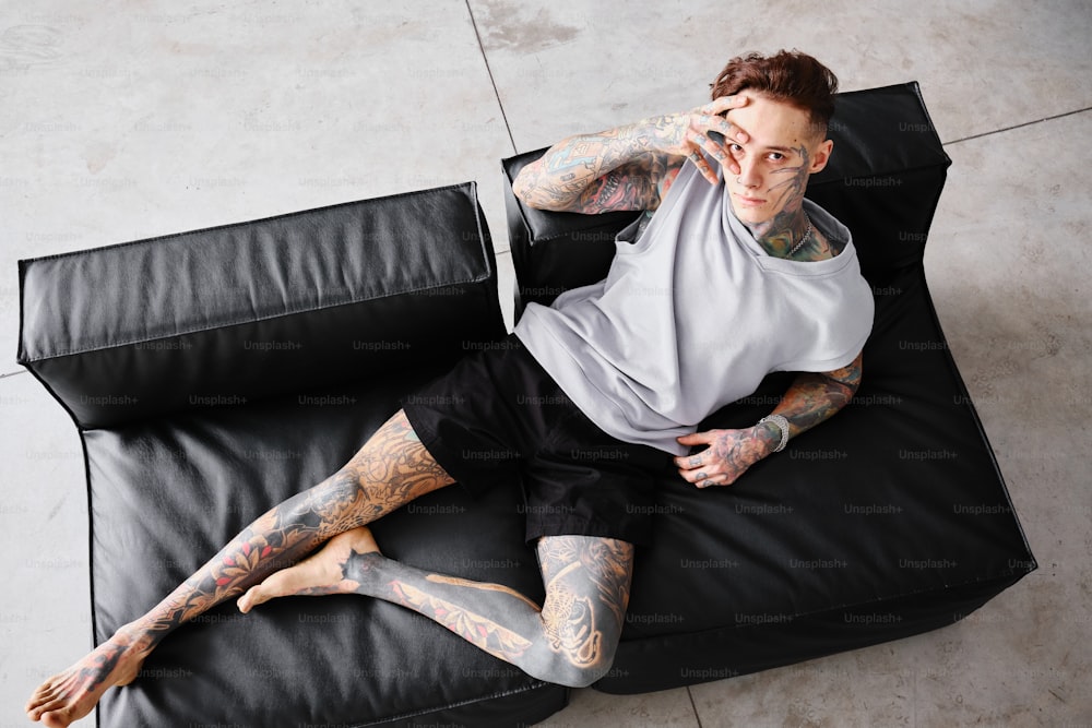 a man with tattoos sitting on a black couch