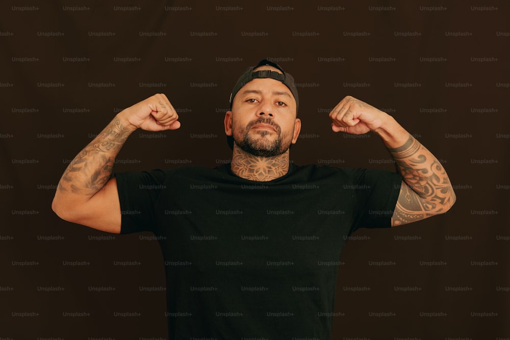 Un hombre con tatuajes y una camisa negra flexiona sus músculos