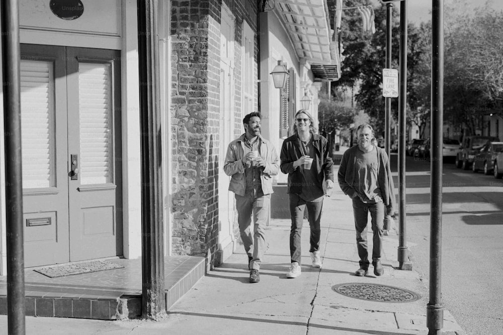 a black and white photo of three people walking down a sidewalk