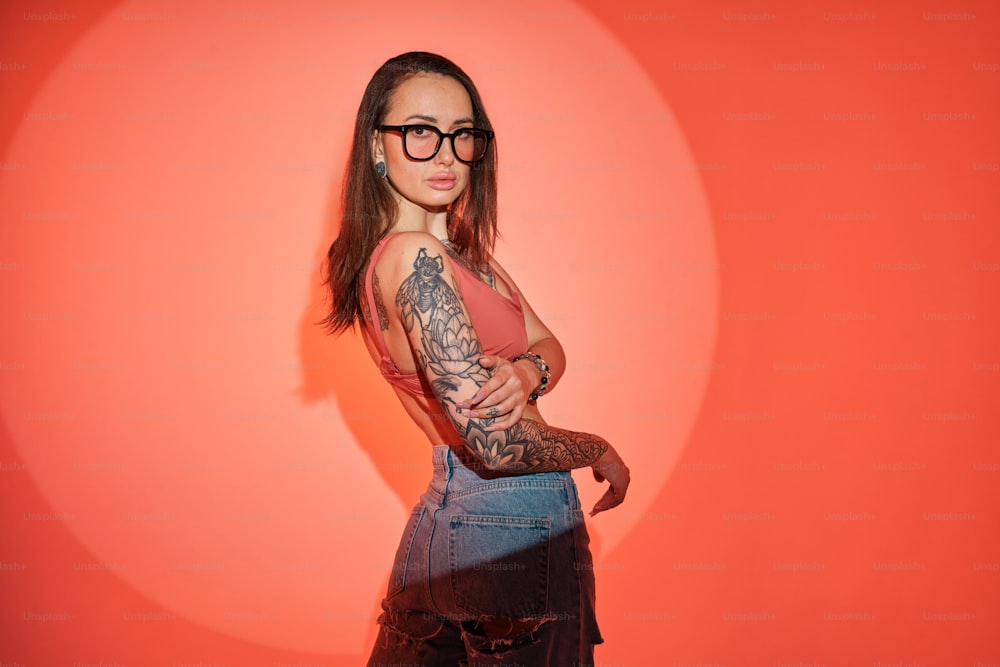 a woman with tattoos and glasses standing in front of a red wall