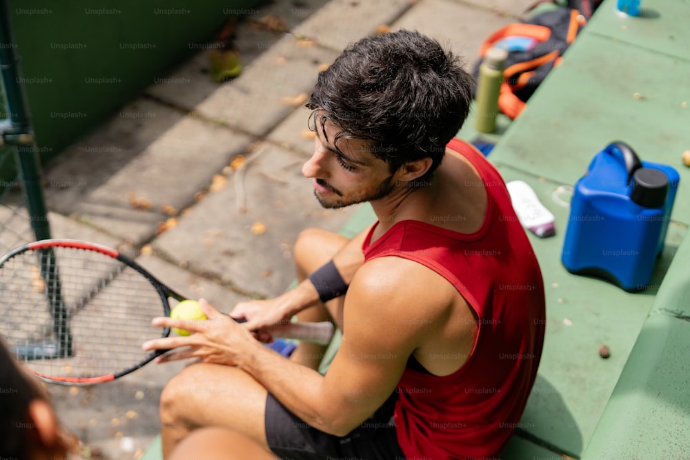 a man sitting on a bench holding a tennis racquet