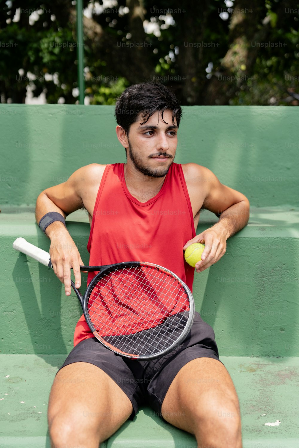 a man sitting on a bench with a tennis racket and ball