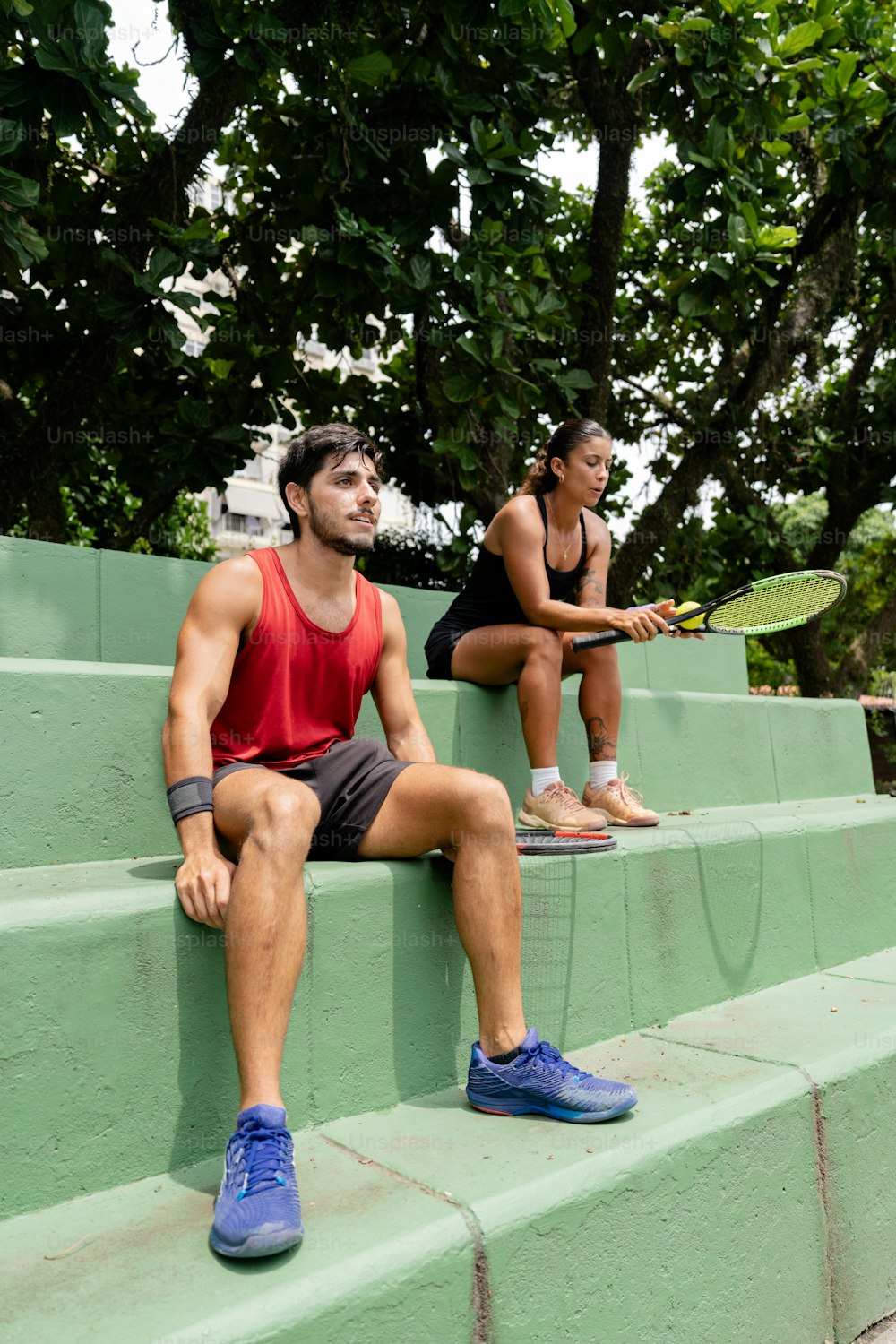 a man and a woman sitting on steps with tennis rackets