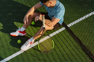 ein Mann sitzt auf einem Tennisplatz und hält einen Schläger in der Hand