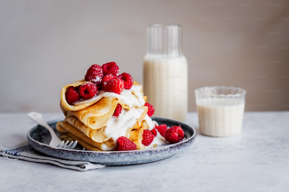 a stack of pancakes topped with whipped cream and raspberries