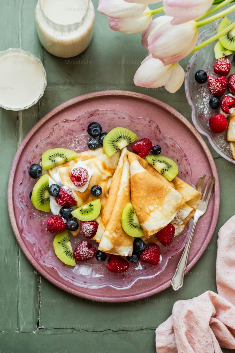 Un plato rosado cubierto de fruta junto a un vaso de leche