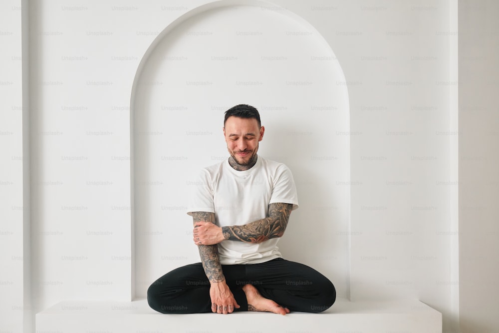 Un hombre con tatuajes sentado en una habitación blanca