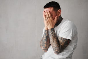 a tattooed man covering his face with his hands