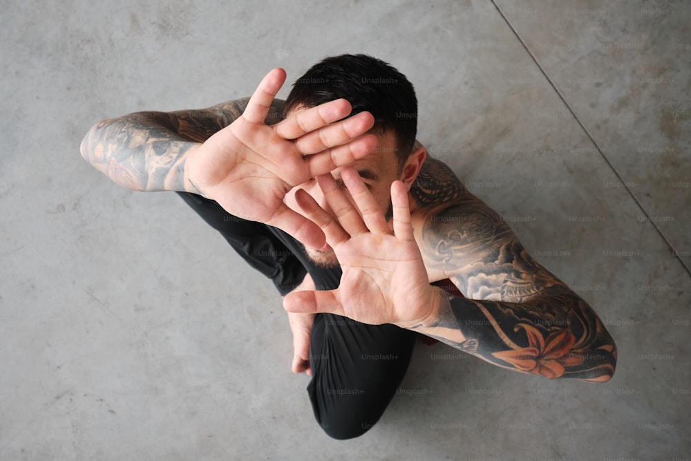 un uomo con tatuaggi che si copre il viso con le mani