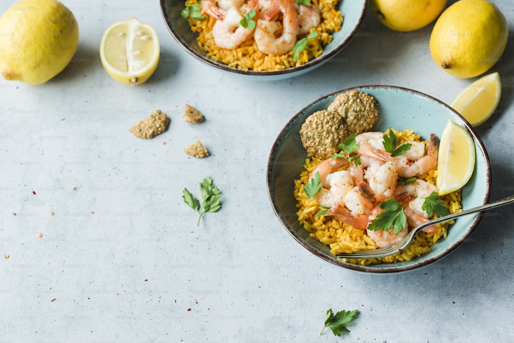 two bowls filled with rice and shrimp next to lemons