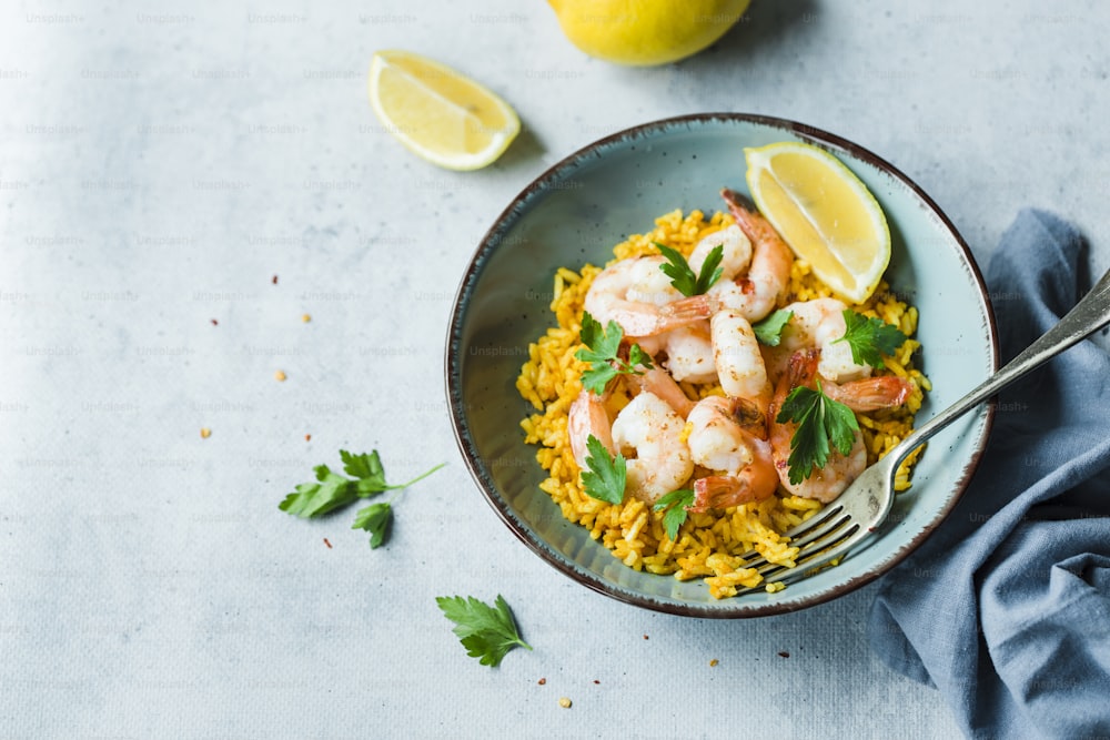 a bowl of shrimp and rice with lemons and parsley