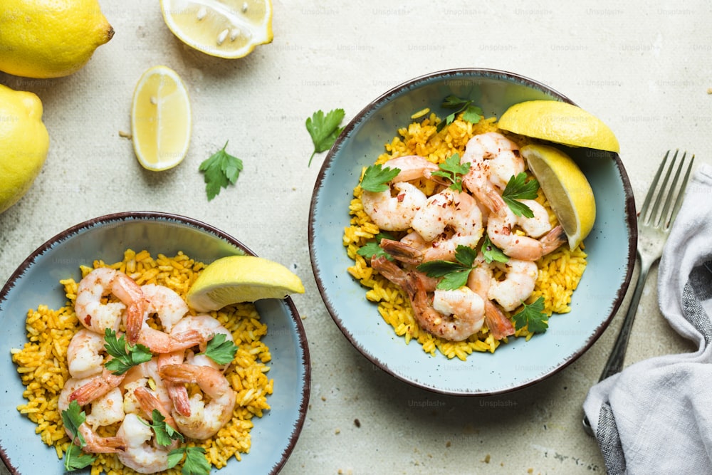 two bowls of shrimp and rice with lemon wedges
