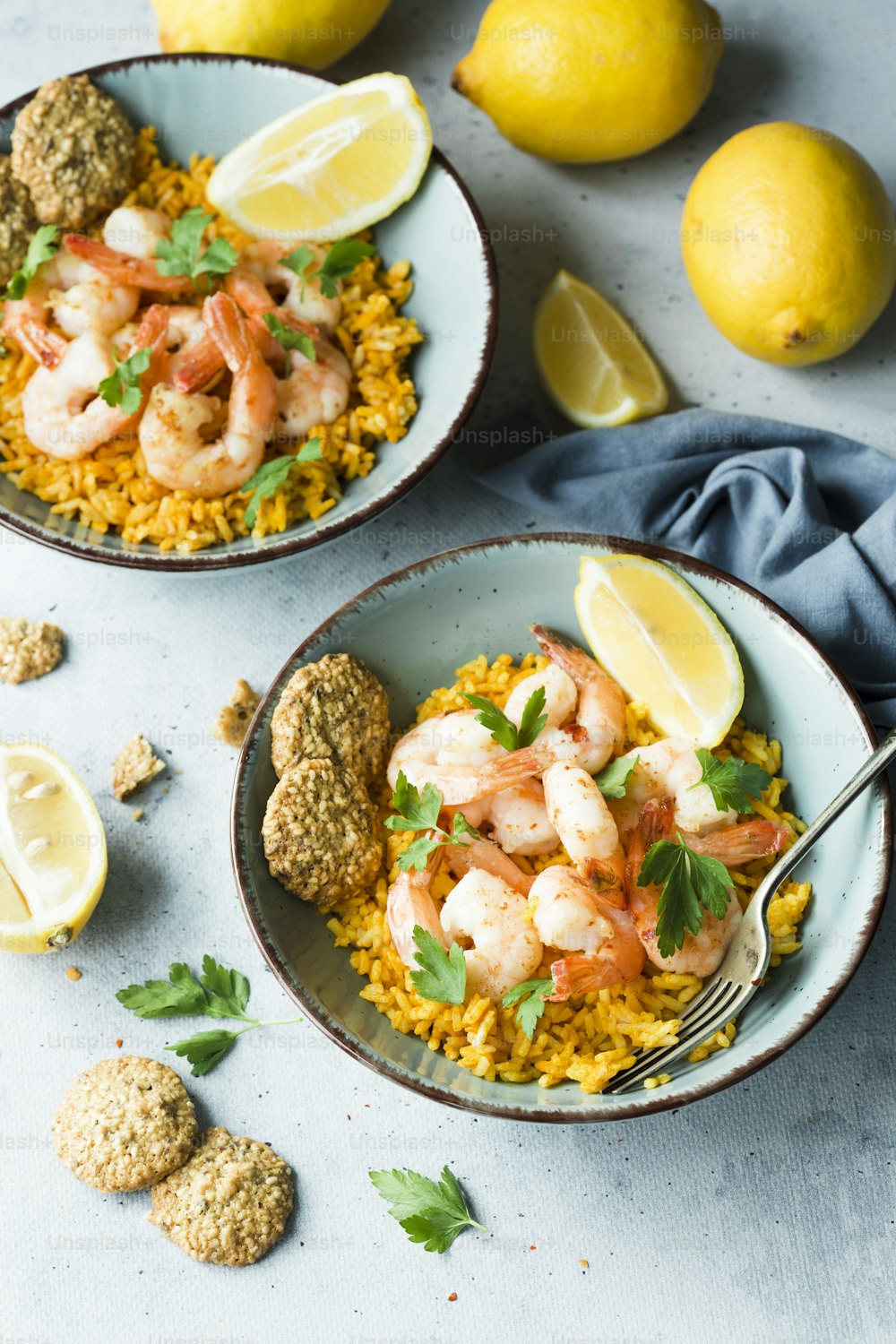 two bowls of shrimp and rice with lemons and parsley