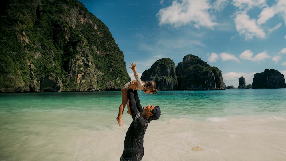 Un hombre sosteniendo a una mujer sobre sus hombros mientras está de pie en el océano
