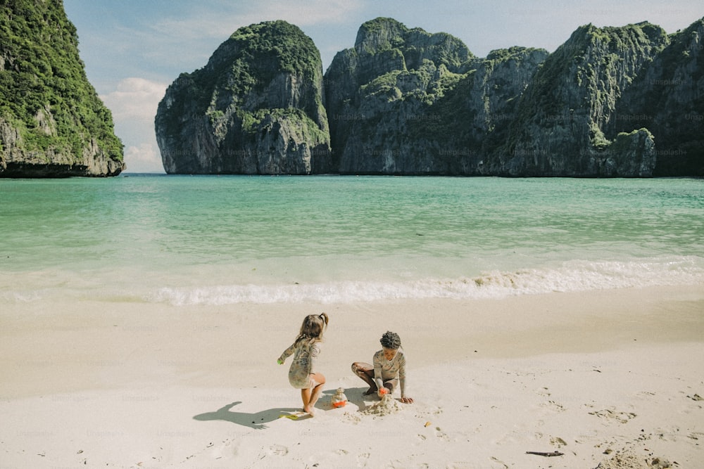 a couple of people sitting on top of a sandy beach