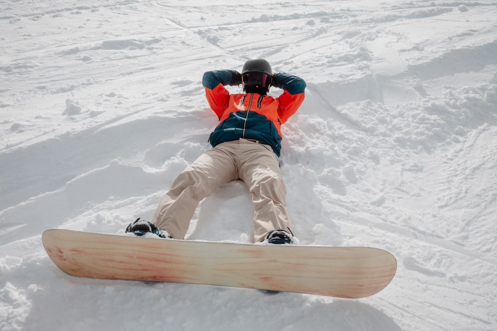 una persona tumbada en la nieve con una tabla de snowboard