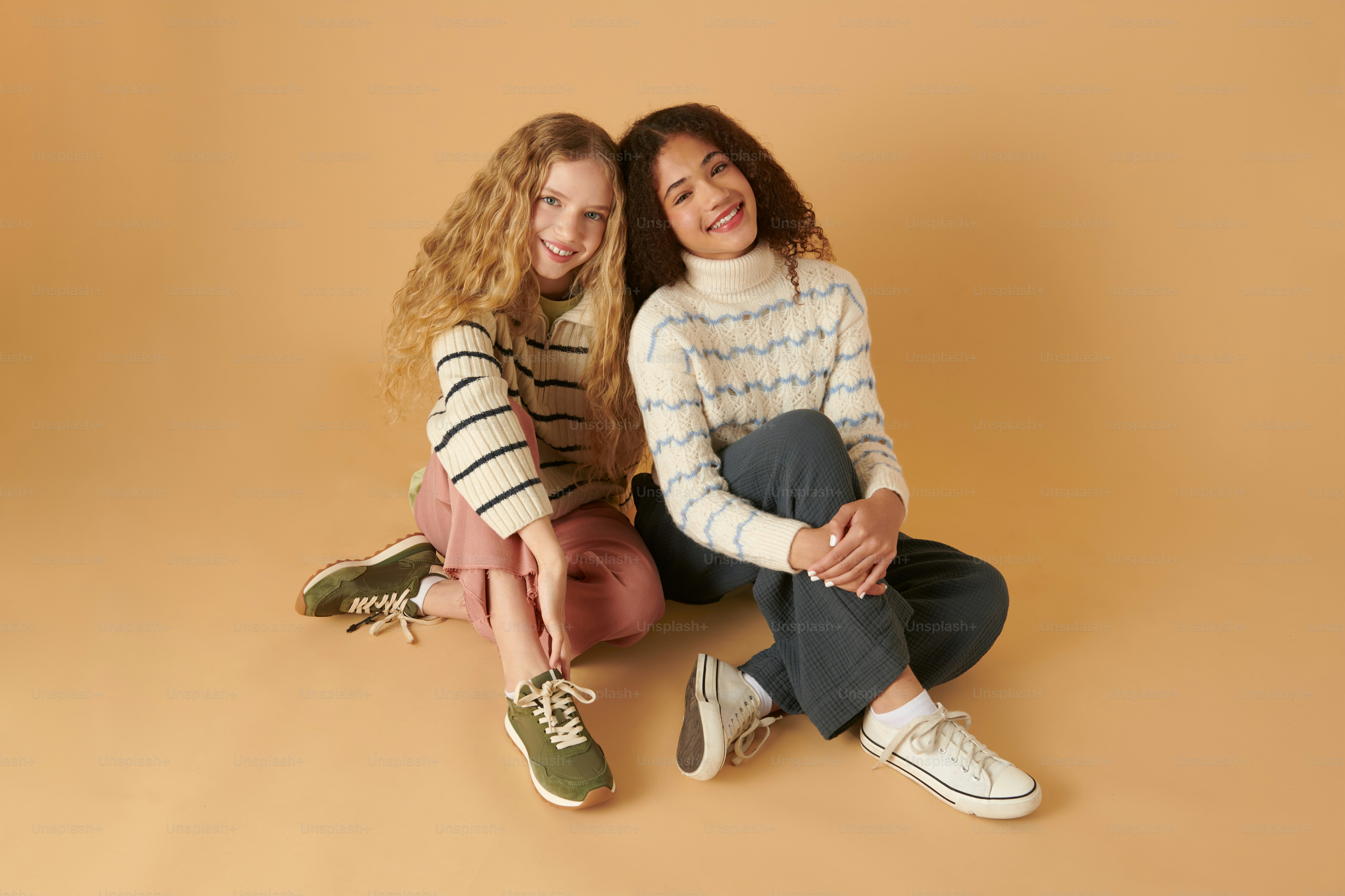 two girls sitting on the ground posing for a picture