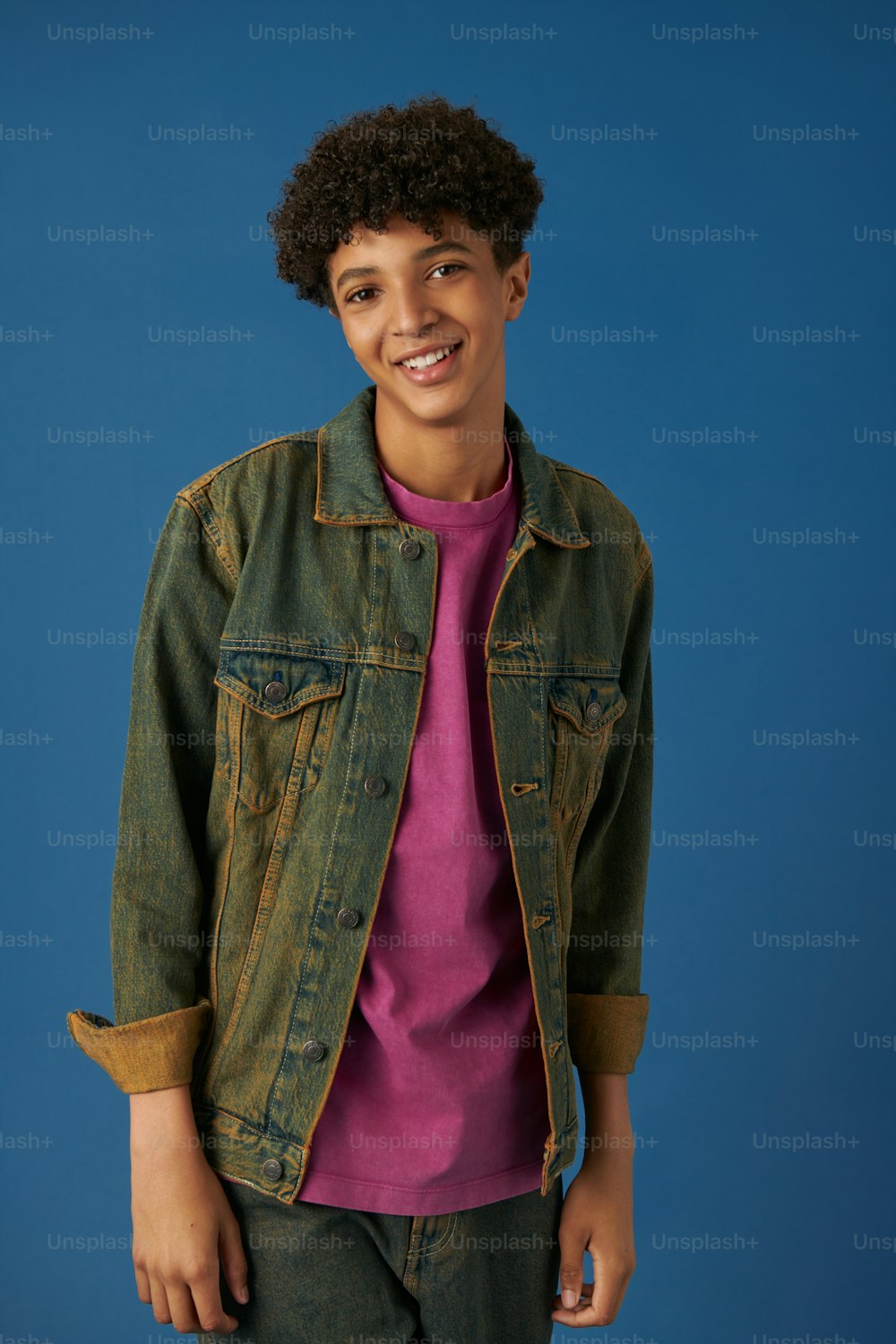 a young man wearing a jean jacket and a pink shirt