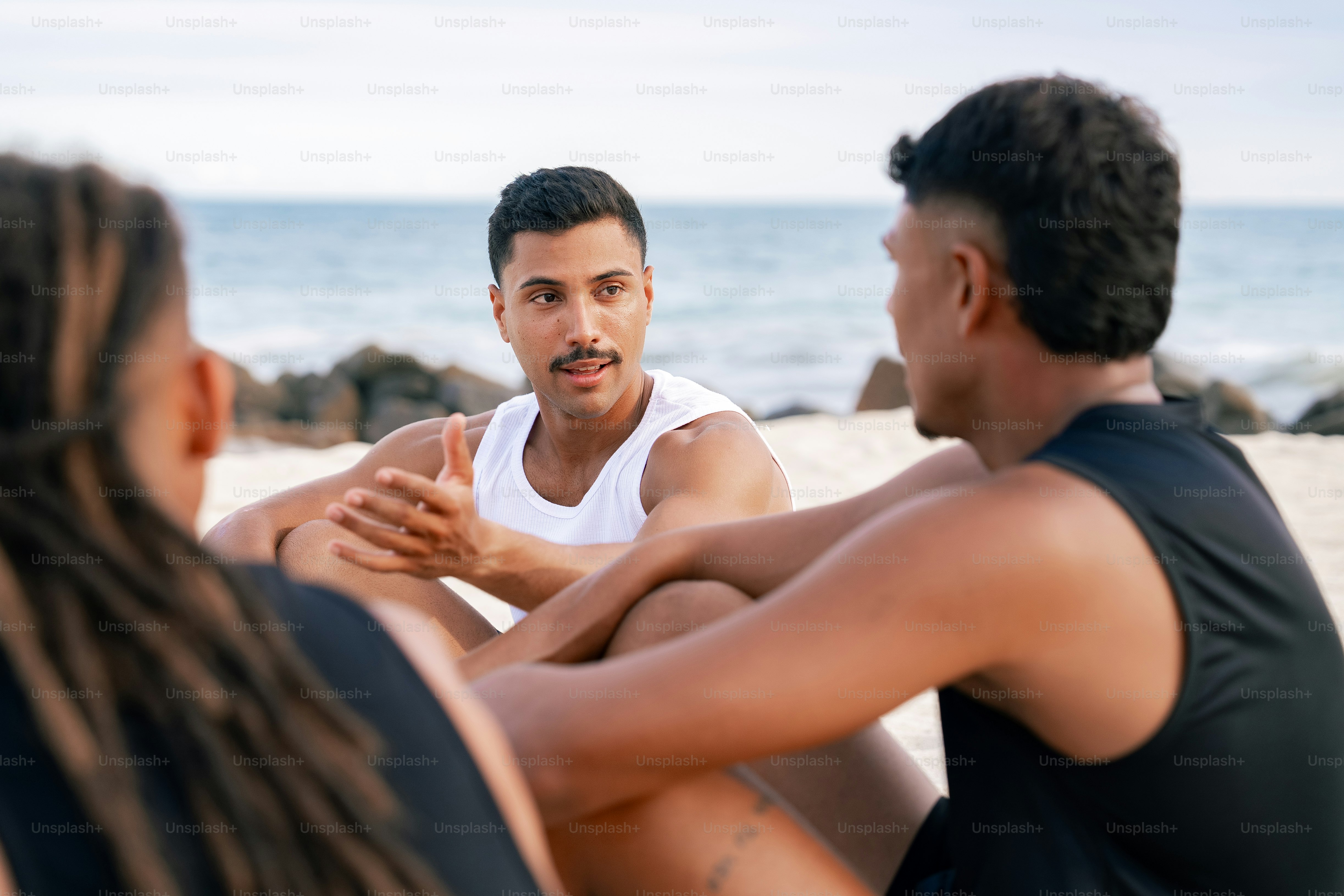 two men and a woman sitting on the beach