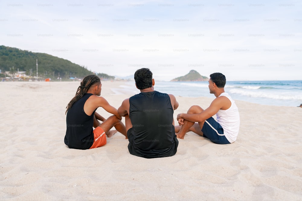 three people sitting on the sand at the beach
