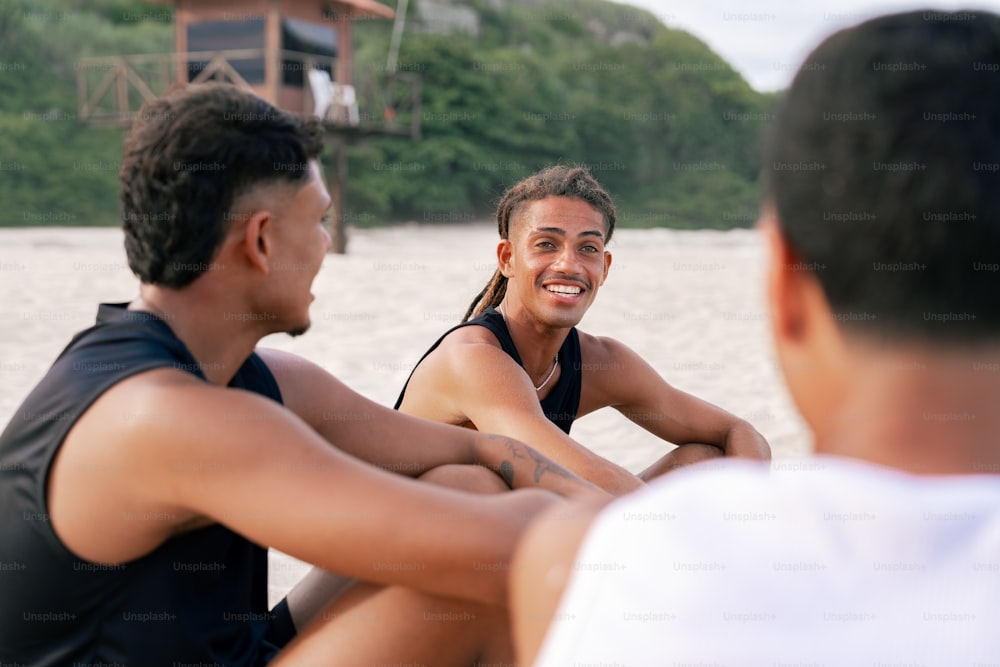 a group of men sitting on top of a sandy beach
