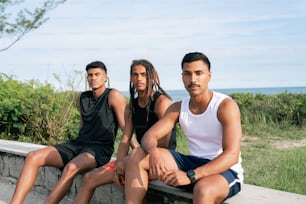 Drei junge Männer sitzen auf einer Steinmauer in der Nähe des Ozeans