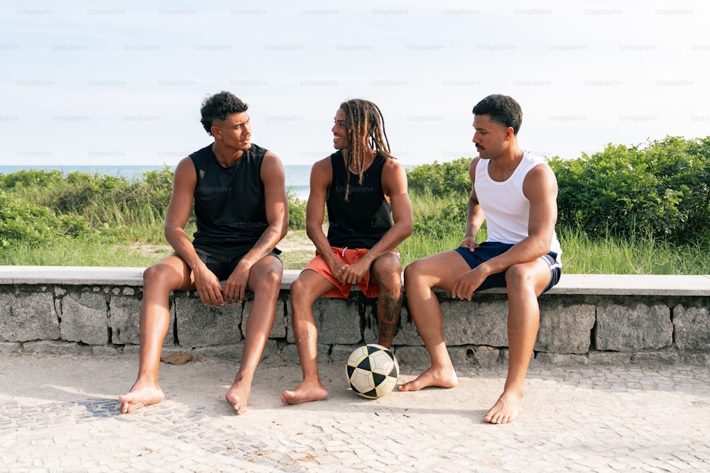 three people sitting on a stone bench with a soccer ball