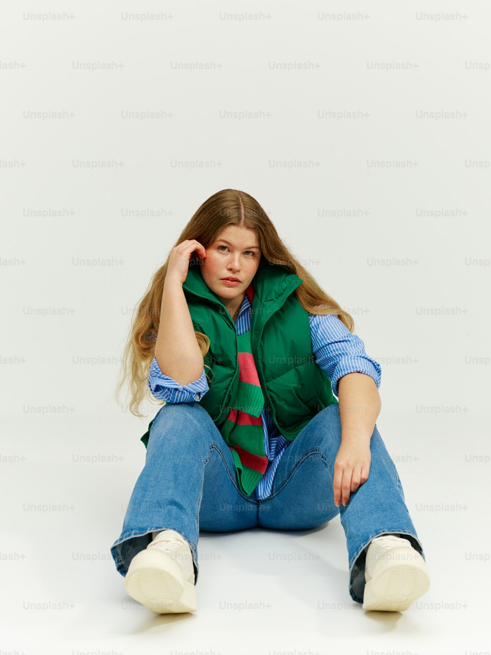 a young girl sitting on the ground wearing a green vest