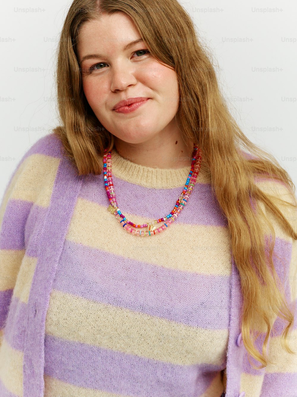 a woman with long hair wearing a sweater and a beaded necklace