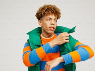 um jovem de cabelos cacheados vestindo uma jaqueta laranja, azul e verde