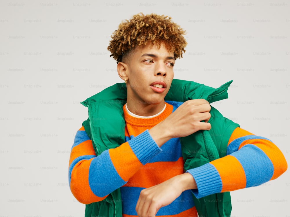 a young man with curly hair wearing an orange, blue, and green jacket