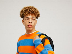 Un joven con cabello rizado que viste un suéter de rayas naranjas y azules