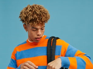 a young man with curly hair wearing an orange and blue striped sweater