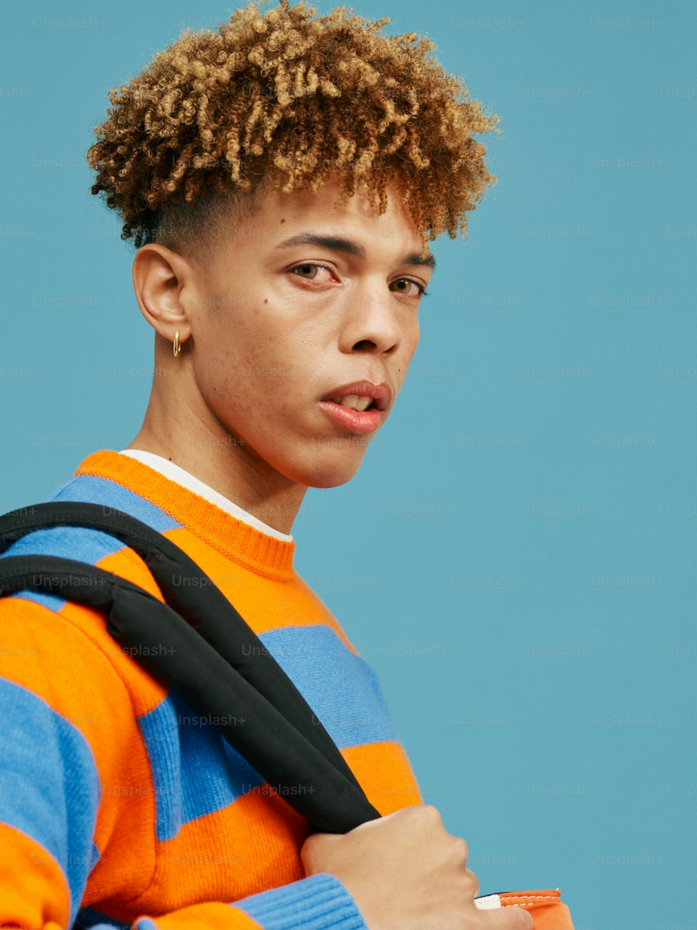 a young man with curly hair holding a backpack