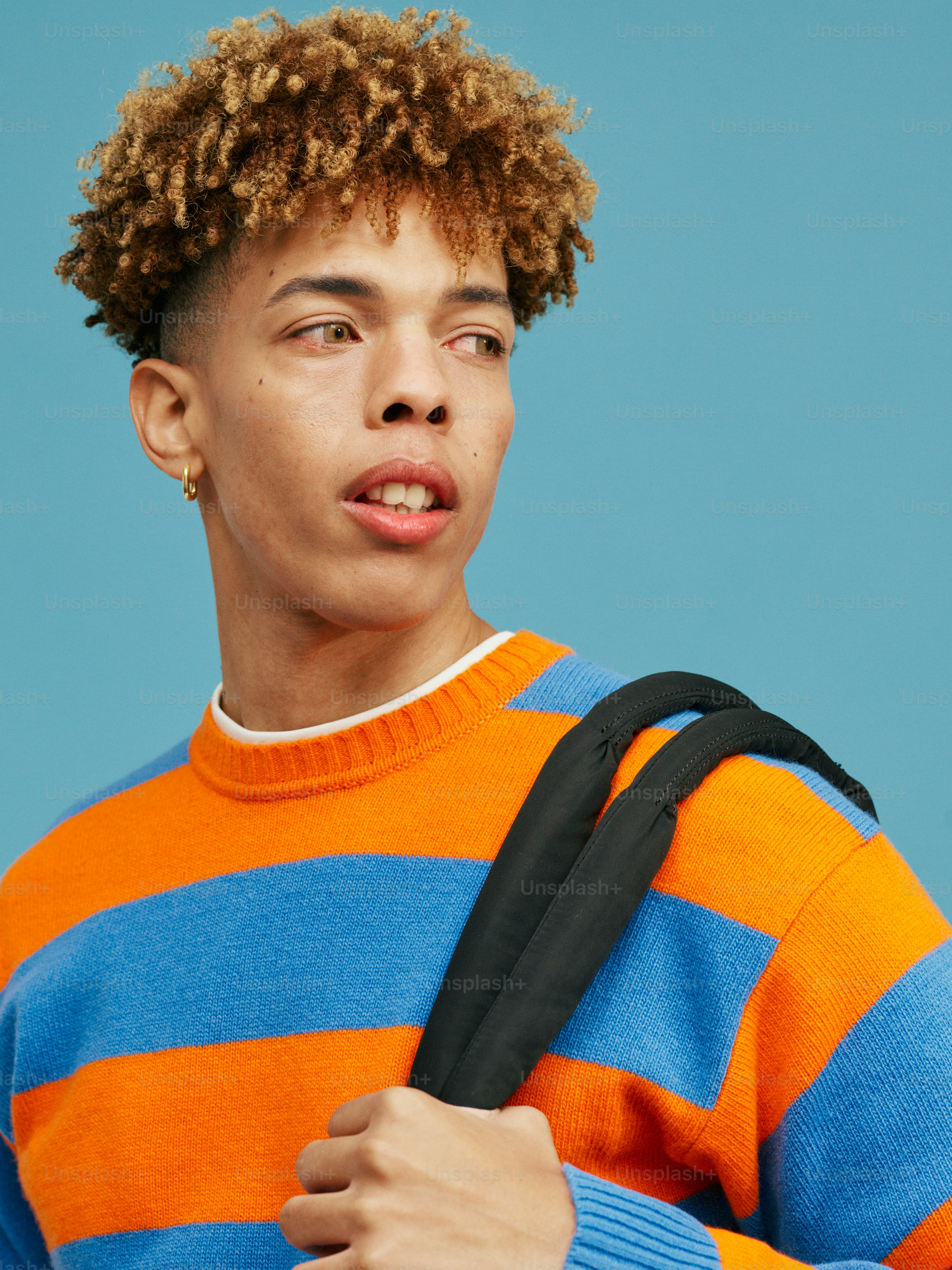 a young man with curly hair holding a black bag