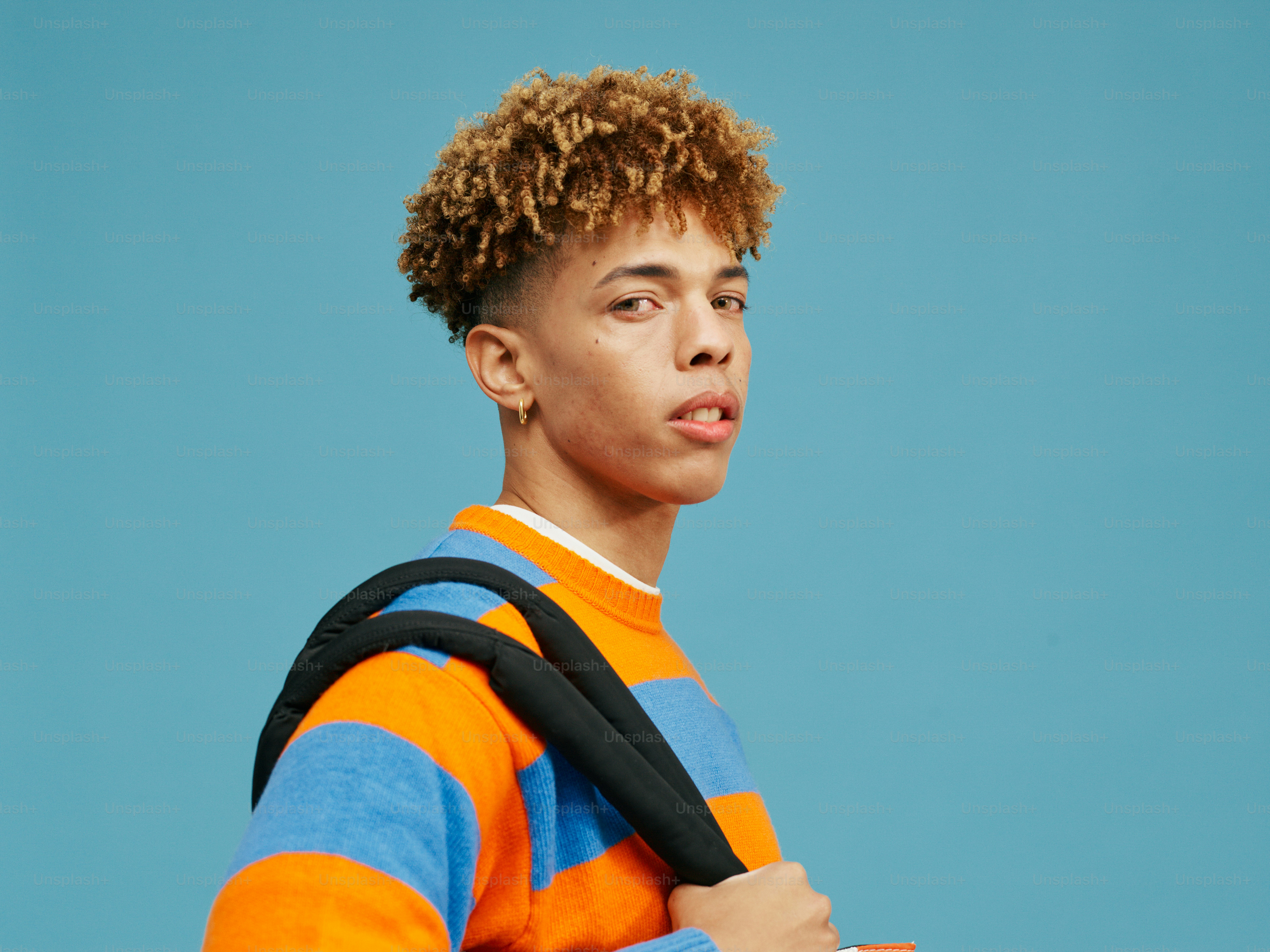 a young man with curly hair wearing a backpack