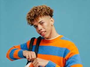a young man with curly hair wearing a blue and orange striped sweater