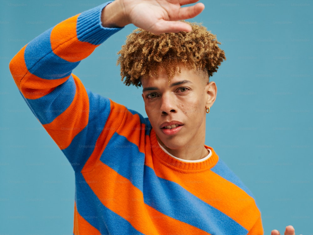 un jeune homme aux cheveux bouclés vêtu d’un pull rayé orange et bleu